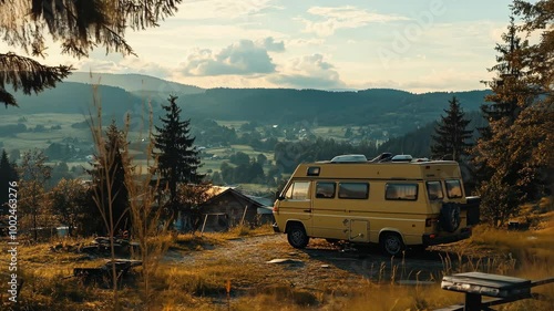 A yellow camper van is parked on a hilltop overlooking a valley and forested mountains in the afternoon