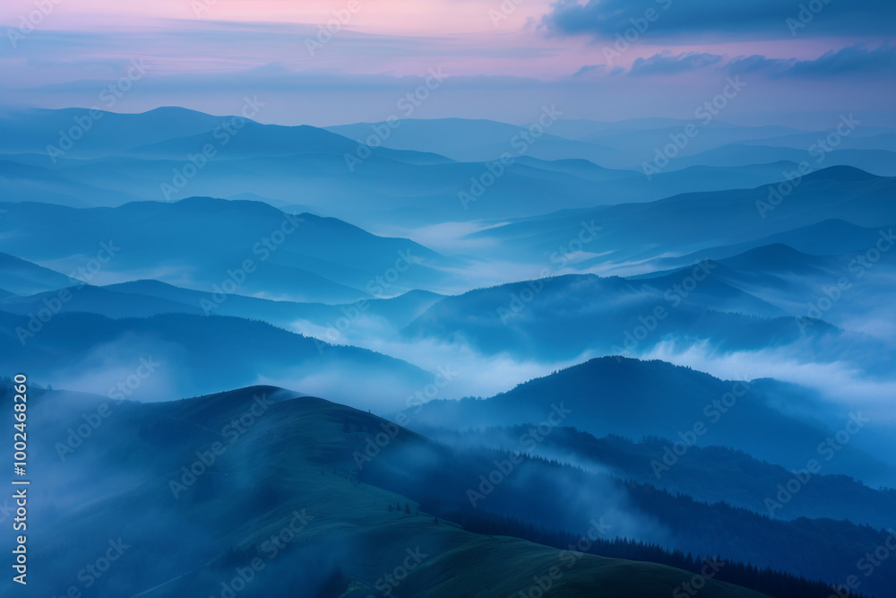 Obraz premium Misty mountain range at dawn with soft blue hues and rolling fog creating a serene landscape