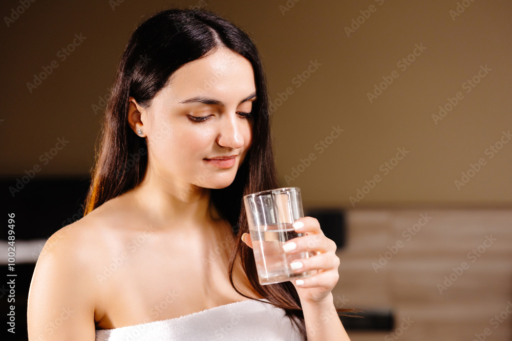 Pretty brunette drinking water standing near bed at home in the bedroom. Pretty brunette drinking water standing near bed at home in the bedroom.