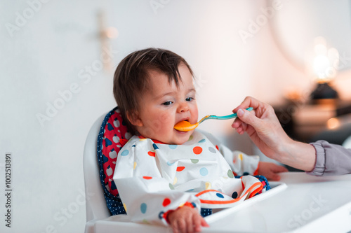 A little baby girl dislikes her healthy meal but in spite of that she is eating somehow	 photo