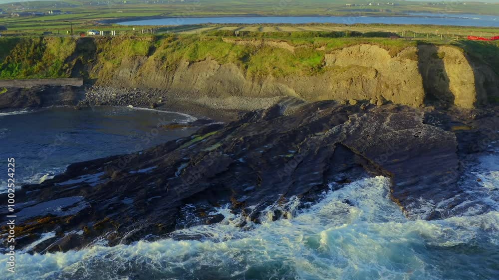 Slow-motion waves crashing on the Irish coast at the Kilkee Cliffs Walk, illuminated by beautiful sunrise light Slow-motion waves crashing on the Irish coast at the Kilkee Cliffs Walk, illuminated by beautiful sunrise light