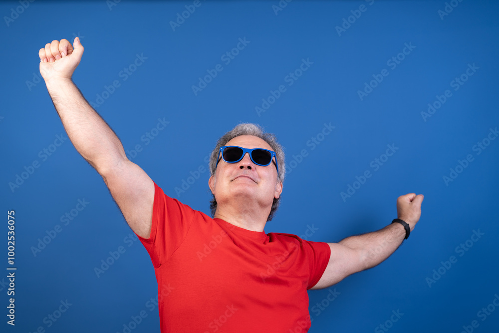 Naklejka premium A man in a red shirt is wearing sunglasses and is raising his arms in the air