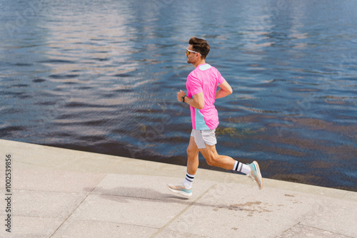 A Young Man Jogging in Bright Pink Attire Along the Riverside Pathway on a Sunny Day