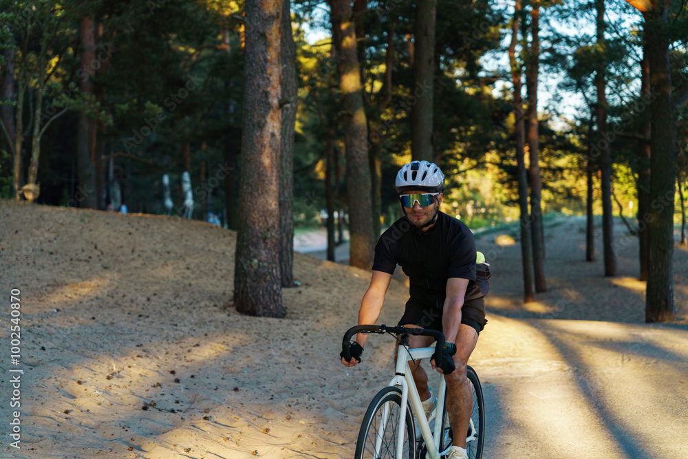 Fototapeta premium A Cyclist Navigates a Sandy Trail Surrounded by Tall Trees During Late Afternoon Light