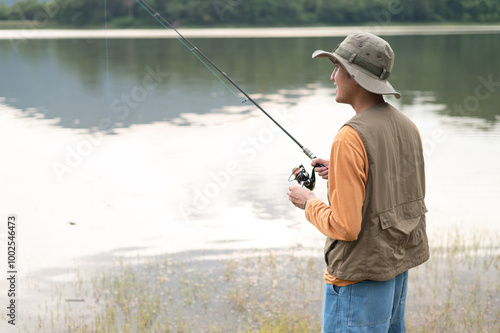 Fisherman man fishing with a spinning fishing rod in hand, close-up on the bank of a river or lake. With the light scene during the sunset against the natural forest in the background Hobby,fisherman.