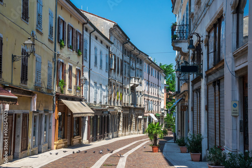 Fototapeta Naklejka Na Ścianę i Meble -  Picturesque narrow street lined with colorful buildings, shuttered windows, and traditional architecture in Gorizia's old town. Decorative lamps and potted plants add to the quaint atmosphere