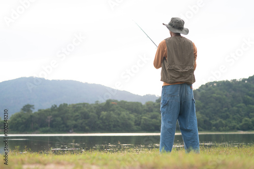 Fisherman man fishing with a spinning fishing rod in hand, close-up on the bank of a river or lake. With the light scene during the sunset against the natural forest in the background Hobby,fisherman.