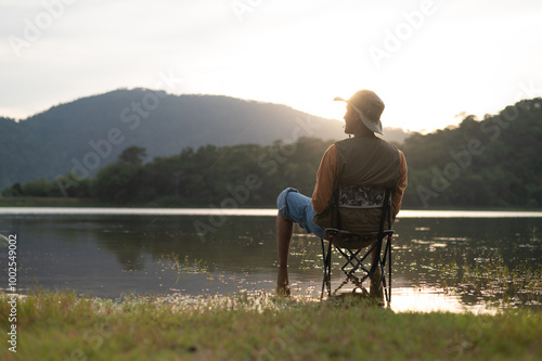 Fisherman man fishing with a spinning fishing rod in hand, close-up on the bank of a river or lake. With the light scene during the sunset against the natural forest in the background Hobby,fisherman.