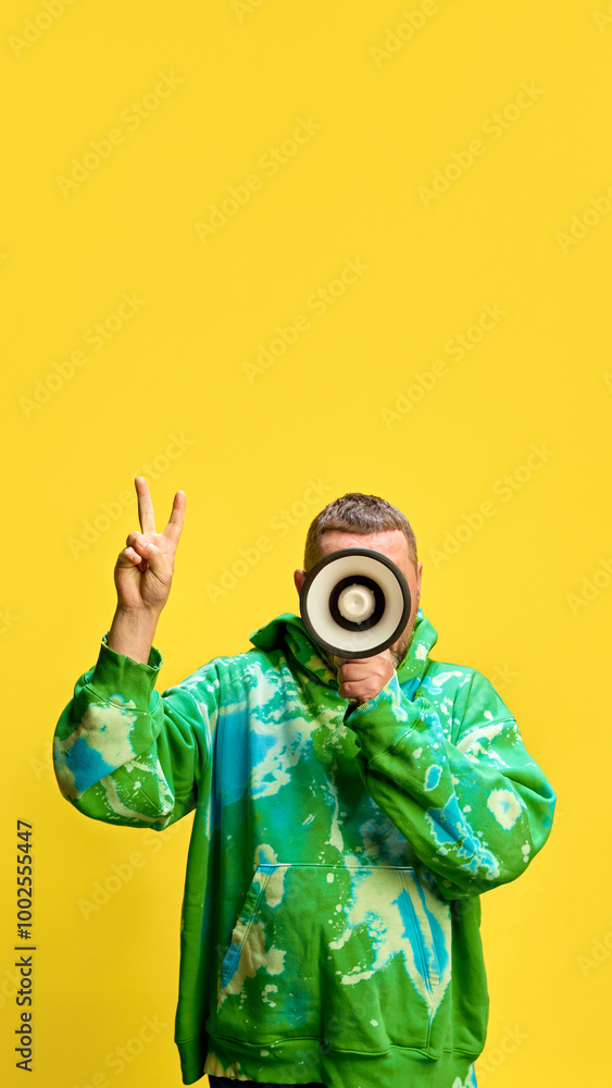 Man in stylish hoodie talking on megaphone against yellow studio background. Discounts for loyal customers, giant sales, good offers. Concept of sales, shopping, news, announcement, advertisement Man in stylish hoodie talking on megaphone against yellow studio background. Discounts for loyal customers, giant sales, good offers. Concept of sales, shopping, news, announcement, advertisement