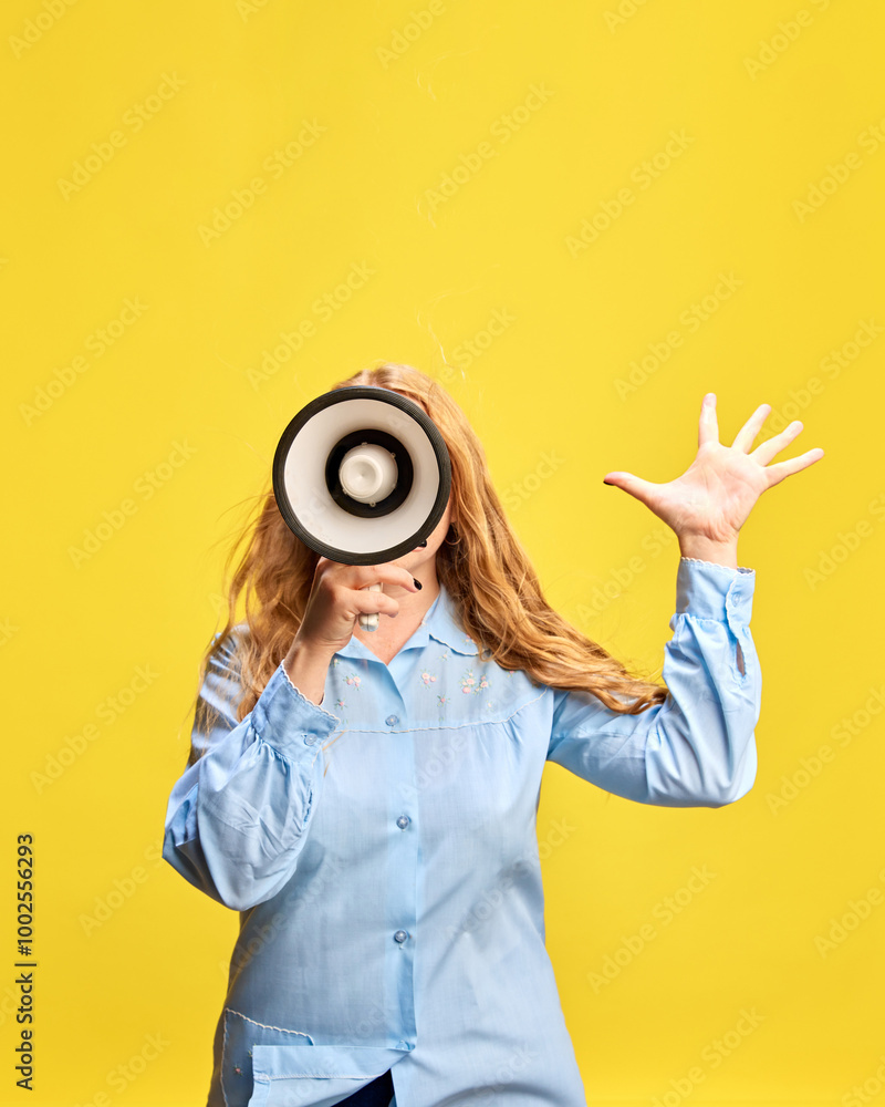 Fototapeta premium Young woman in blue shirt with megaphone against yellow studio background. Seasonal sale Announcement, promotion of weekly specials. Concept of sales, shopping, news, advertisement