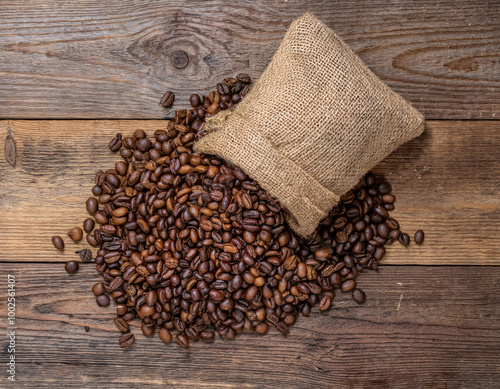 A rustic burlap sack filled with roasted coffee beans spills onto a weathered wooden table, creating a warm and earthy visual that highlights the natural textures.