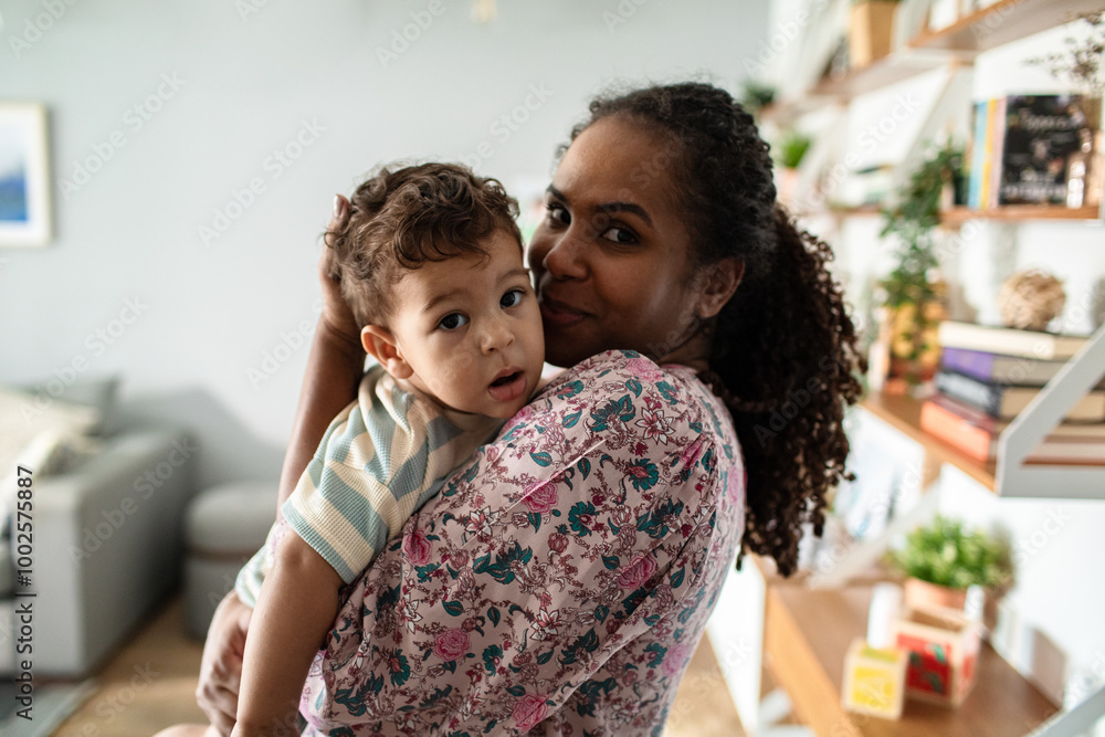 Portrait of a young mother holding toddler son in modern home looking at camera