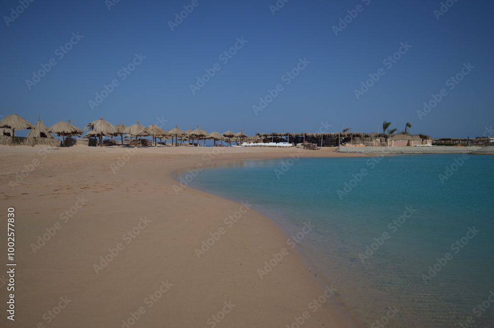 The blue water of the Red Sea in Egypt, a wide sandy beach when there are no tourists, thatched umbrellas, bungalows and folding sunbeds The blue water of the Red Sea in Egypt, a wide sandy beach when there are no tourists, thatched umbrellas, bungalows and folding sunbeds