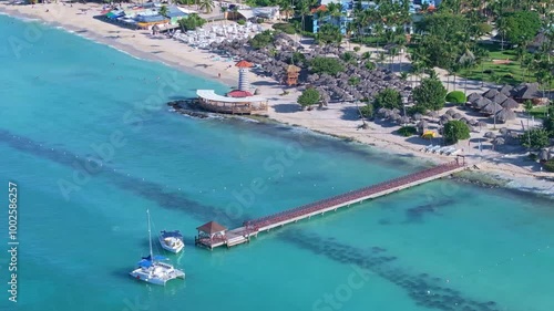 Catamaran boat reaching pier of Playa Dominicus in Bayahibe. Sunny day with clear Caribbean Sea at Iberostar resort with beach and palm trees. Aerial top down shot. photo