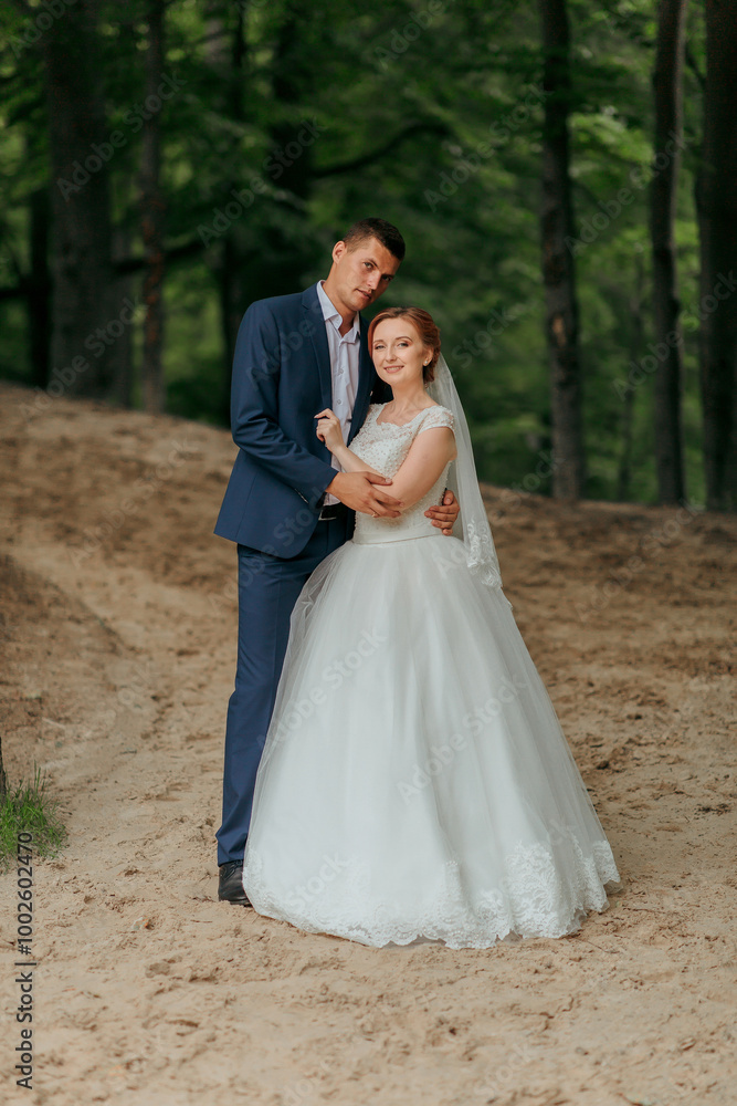 A bride and groom are posing for a picture in a forest. The bride is wearing a white dress and the groom is wearing a blue suit. Scene is happy and romantic A bride and groom are posing for a picture in a forest. The bride is wearing a white dress and the groom is wearing a blue suit. Scene is happy and romantic