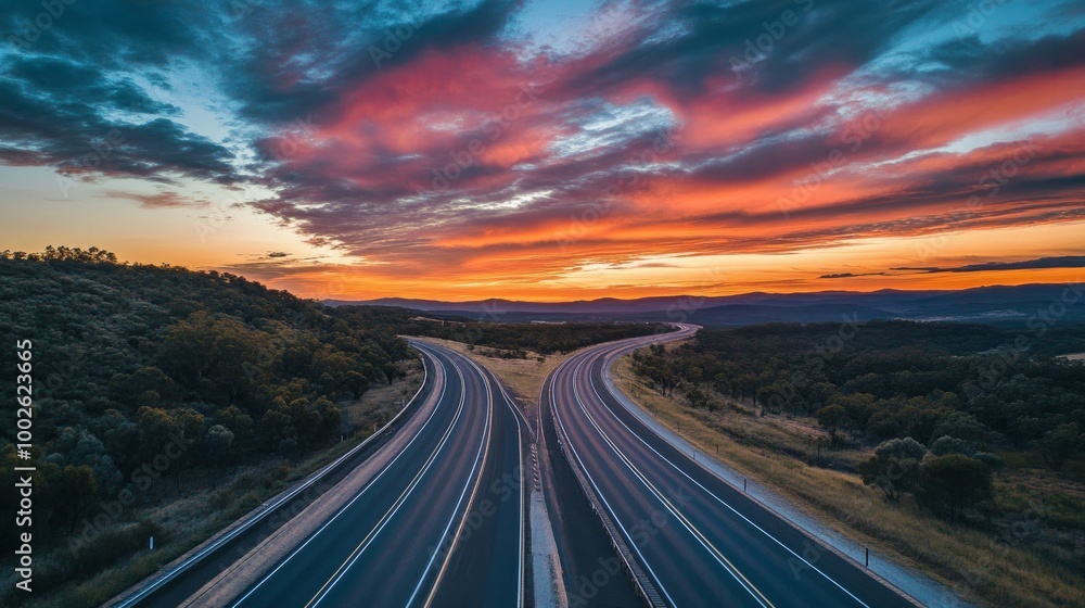 A multi-lane highway situated in the Australian outback, framed by colorful clouds and a vivid evening sky A multi-lane highway situated in the Australian outback, framed by colorful clouds and a vivid evening sky