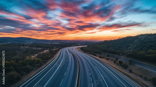 A multi-lane highway situated in the Australian outback, framed by colorful clouds and a vivid evening sky