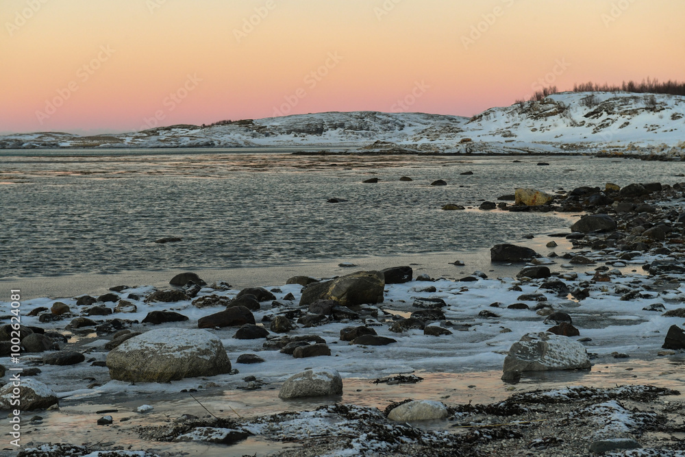 A bright orange glow colours the golden hour sky that serves as a dramatic background for the rugged mountains and snow-covered beaches of arctic norway, near the town of Bodo. A bright orange glow colours the golden hour sky that serves as a dramatic background for the rugged mountains and snow-covered beaches of arctic norway, near the town of Bodo.