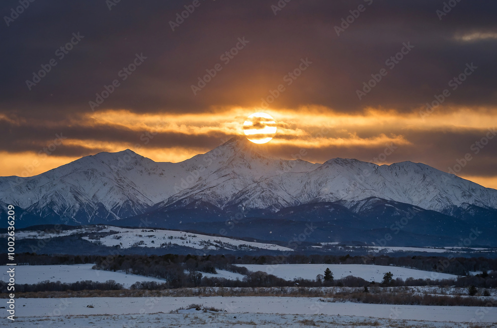Winter solstice sun setting behind snowy mountains, symbolizing seasonal change Winter solstice sun setting behind snowy mountains, symbolizing seasonal change
