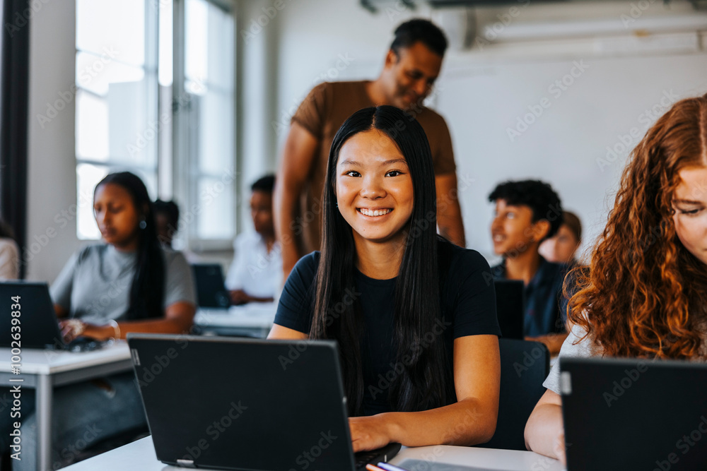 Portrait of smiling teenage student sitting with laptop in classroom at junior high school Portrait of smiling teenage student sitting with laptop in classroom at junior high school