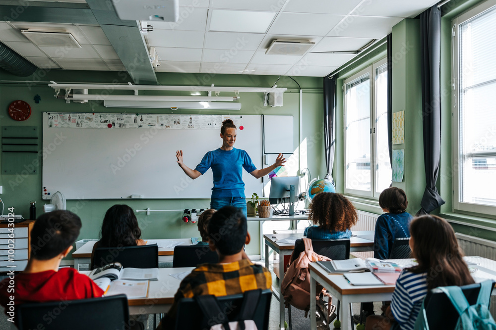 Female professor with arms outstretched teaching group of students in classroom at elementary school Female professor with arms outstretched teaching group of students in classroom at elementary school