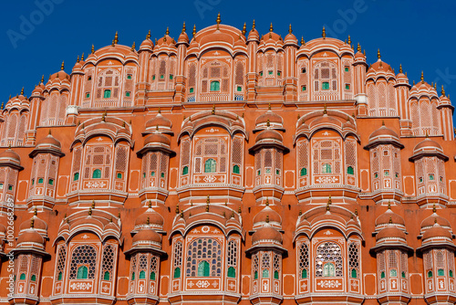 A detailed close-up of the Hawa Mahal’s facade in Jaipur, highlighting its intricate latticework, arched windows, domed canopies, vibrant red sandstone, and green accents.  photo