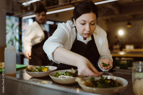 Focused female chef garnishing salad with cilantro in commercial kitchen photo