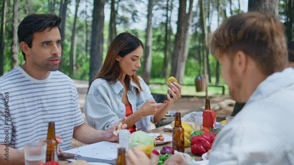 Young group enjoying lunch at picnic table surrounded by greenery summer forest. Young group enjoying lunch at picnic table surrounded by greenery summer forest.