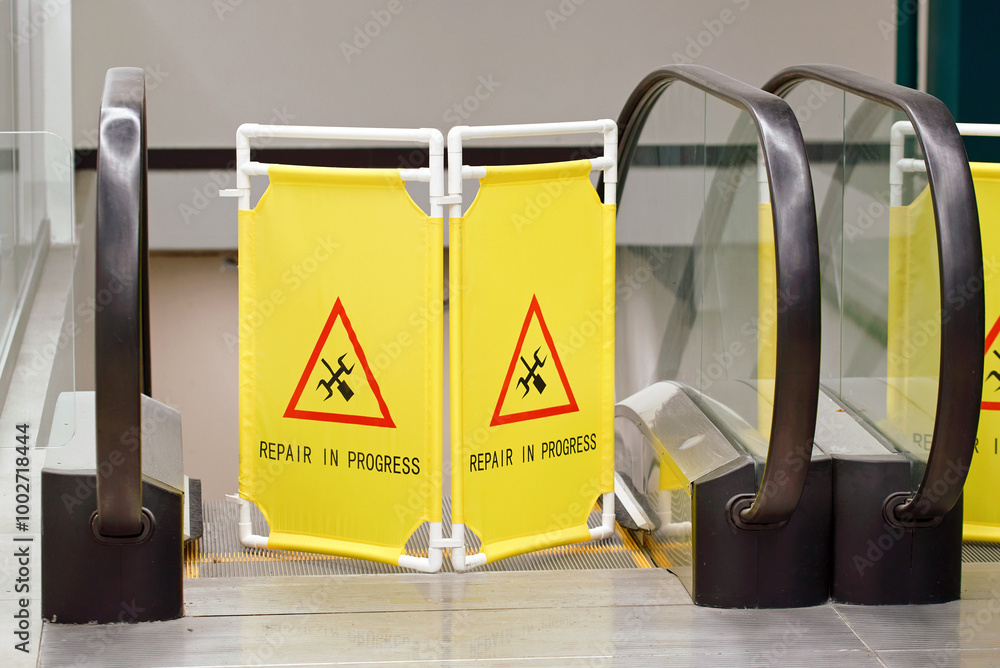 Repair in progress sign displayed in front of an escalator or travelator in shopping center, maintenance work, public safety near the travelator. Warning barrier blocking escalator for maintenance