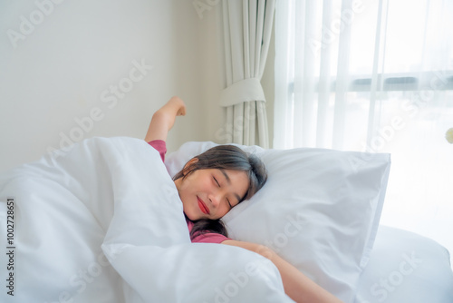 Asian young woman stretching body while lying down on bed in bedroom at home. Teenager girl wake up with happiness enjoying morning early in house.