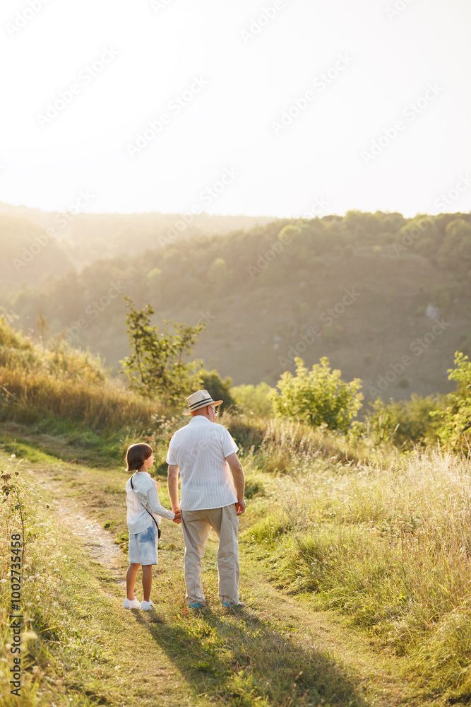Backside photo of a little boy with his grandfather walking in a field at summer Backside photo of a little boy with his grandfather walking in a field at summer