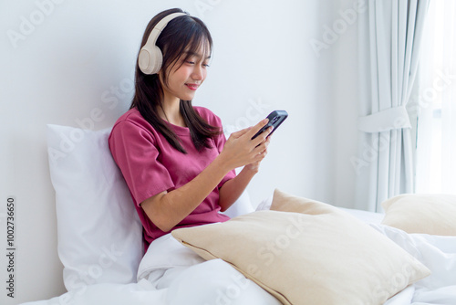 Asian young girl listening music with wireless headphones while sitting on bed.  photo