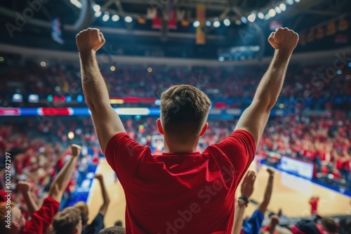 Vibrant red-clad man raises arms in triumph amidst a sea of cheering fans in a packed basketball arena. The elevated angle provides a unique perspective on the electrifying scene.