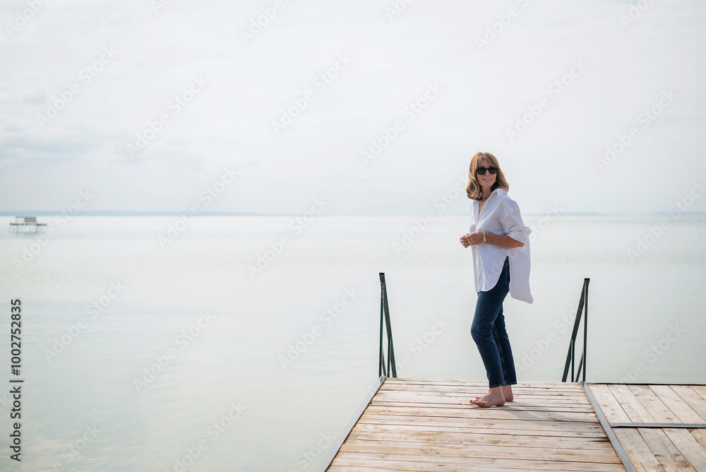 Full length of a blond haired woman standing on the pier by the lake Full length of a blond haired woman standing on the pier by the lake