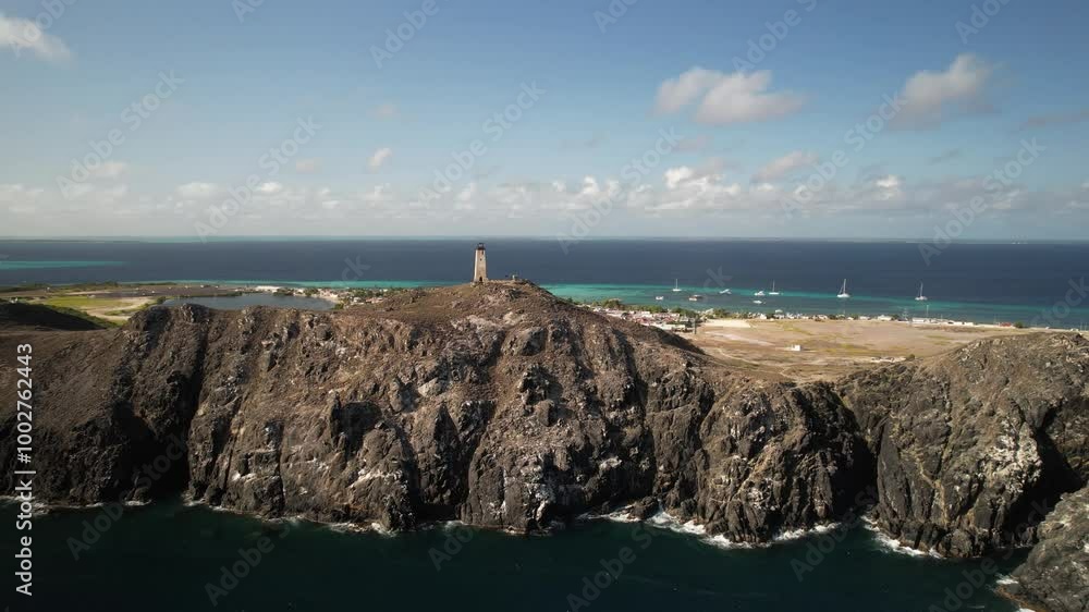 A rugged coastline with a lighthouse on a rocky hill and boats in the turquoise ocean, aerial view A rugged coastline with a lighthouse on a rocky hill and boats in the turquoise ocean, aerial view