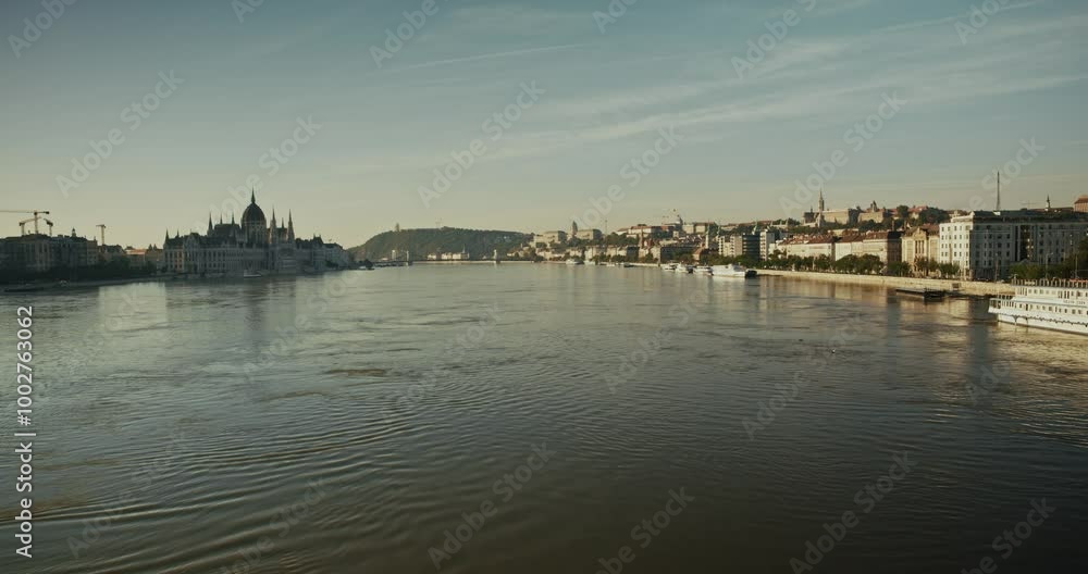 river flooding the banks of Budapest, showing distant Parliament and riverside buildings under a calm, overcast sky river flooding the banks of Budapest, showing distant Parliament and riverside buildings under a calm, overcast sky