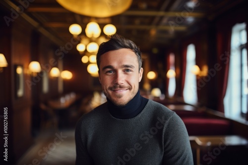 Portrait of a grinning man in his 20s wearing a classic turtleneck sweater while standing against scandinavian-style interior background