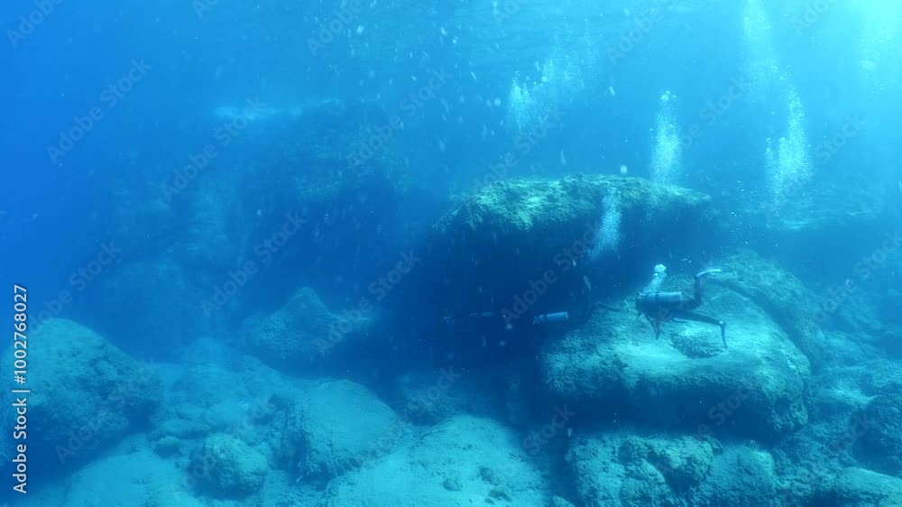 scuba divers exploring around a reef underwater deep blue water big rocks and bubbles ocean scenery scuba divers exploring around a reef underwater deep blue water big rocks and bubbles ocean scenery