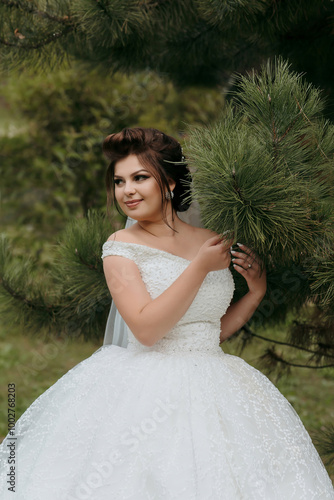 A woman in a white dress is standing in a forest. She is holding a pine tree branch