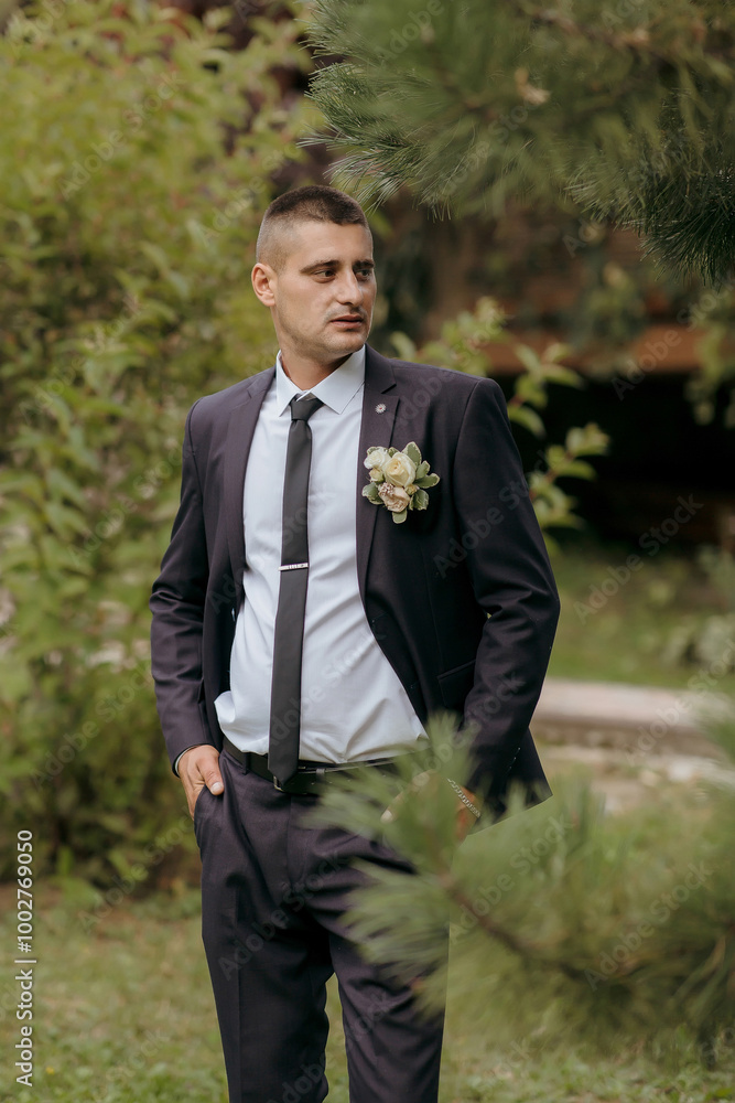 A man in a suit and tie stands in a forest. He is wearing a flower in his lapel A man in a suit and tie stands in a forest. He is wearing a flower in his lapel