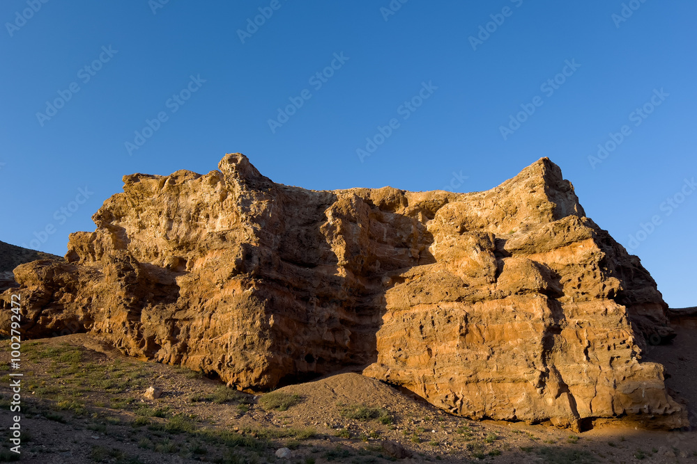 A large formation of rock illuminated by the sun from the side against a blue sky A large formation of rock illuminated by the sun from the side against a blue sky