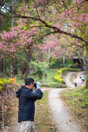 Vertical image Asian man use professional digital camera take a photo. Smiling male photographer look at photo film camera outdoors. Man shooting photo in green nature park. Men hobby lifestyle