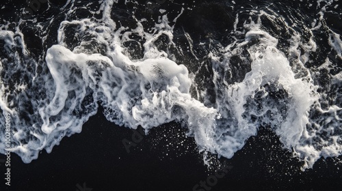 A close-up shot of a wave breaking on a black sand beach, with the dark sand contrasting sharply with the white foam of the wave
