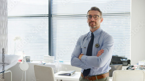 Portrait Of Mature Male Doctor Wearing Stethoscope Standing By Desk In Office Or Surgery