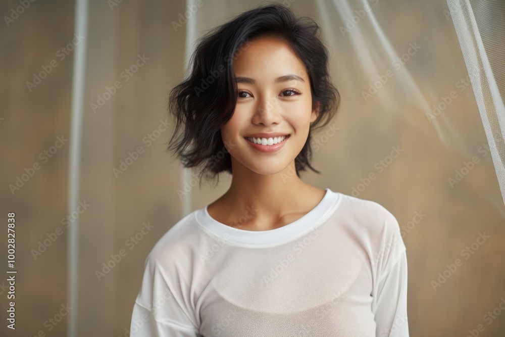 Portrait of a smiling asian woman in her 20s sporting a breathable mesh jersey while standing against bare monochromatic room Portrait of a smiling asian woman in her 20s sporting a breathable mesh jersey while standing against bare monochromatic room