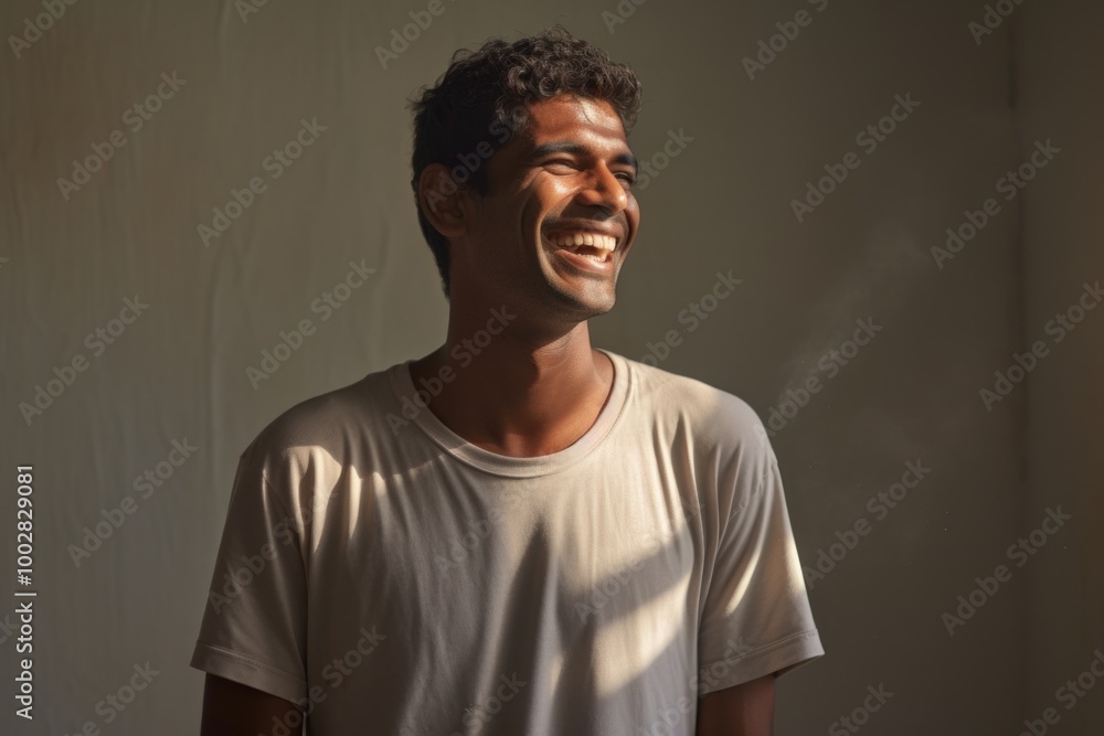 Fototapeta premium Portrait of a grinning indian man in his 20s sporting a long-sleeved thermal undershirt isolated in bare monochromatic room