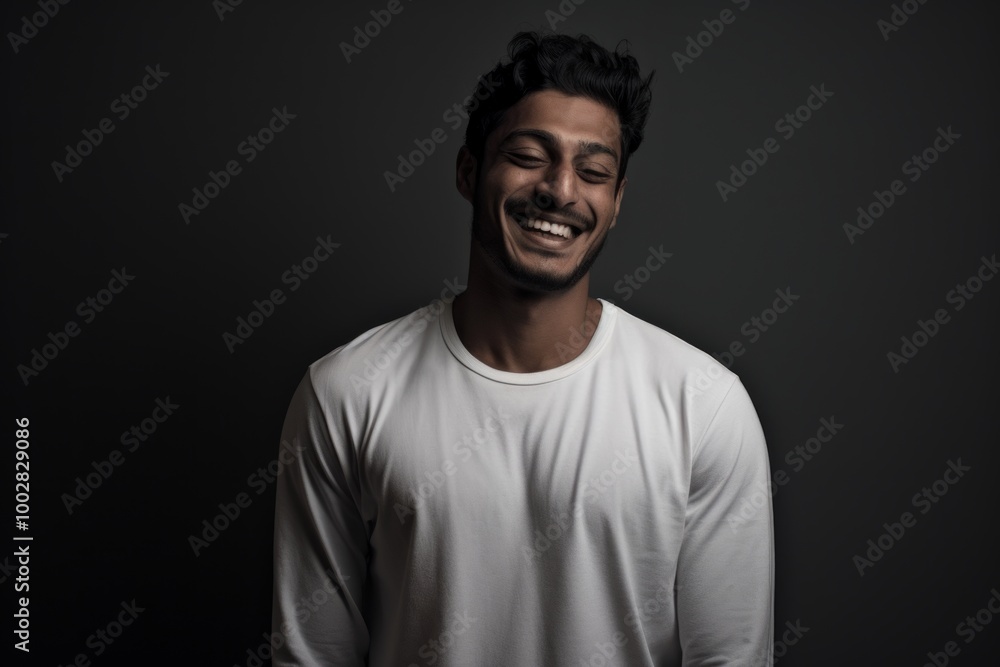 Portrait of a grinning indian man in his 20s sporting a long-sleeved thermal undershirt in front of bare monochromatic room Portrait of a grinning indian man in his 20s sporting a long-sleeved thermal undershirt in front of bare monochromatic room