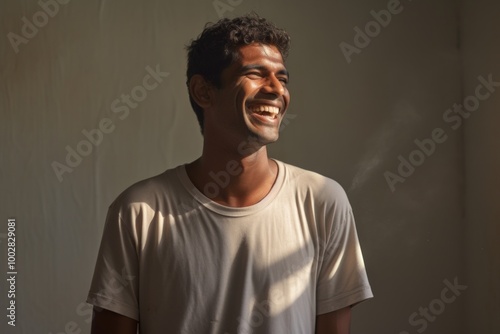 Portrait of a grinning indian man in his 20s sporting a long-sleeved thermal undershirt isolated in bare monochromatic room