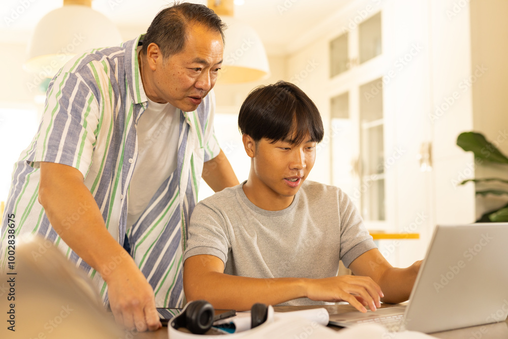 Asian father and teenage son using laptop together at home, focusing on work Asian father and teenage son using laptop together at home, focusing on work