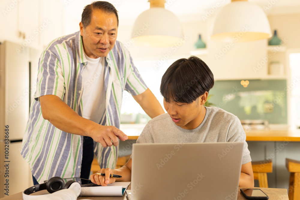 Asian father pointing at laptop while son working on school project at home Asian father pointing at laptop while son working on school project at home